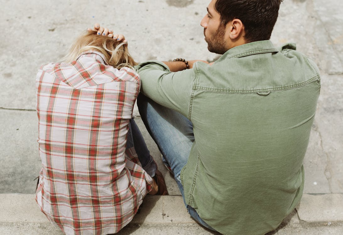 A couple sits on the sidewalk.